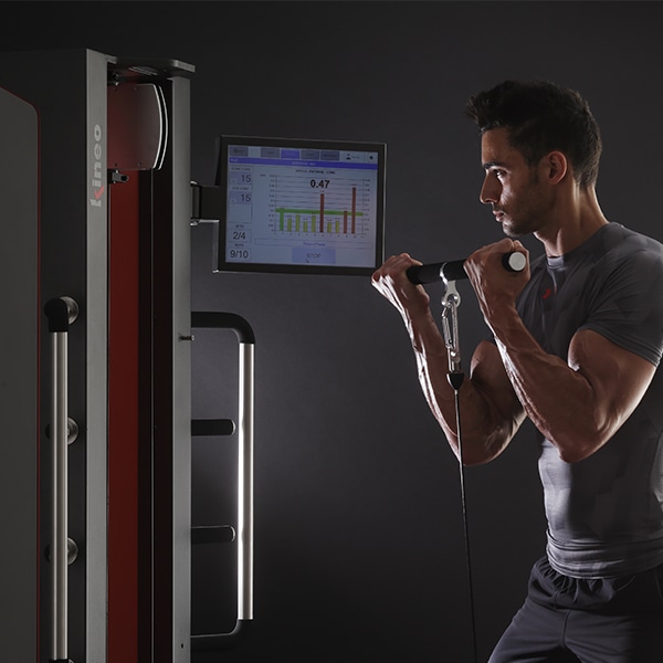 Мужчина тянет канат Kineo Multistation стоя, перед ним экран с графиком усилия