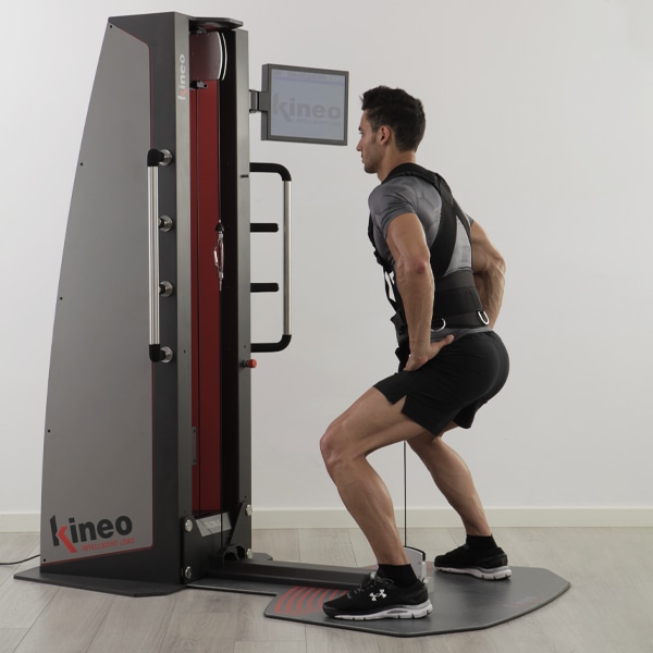 Мужчина приседает на платформе Kineo Pulley & Squat, держа рукоятки каната
