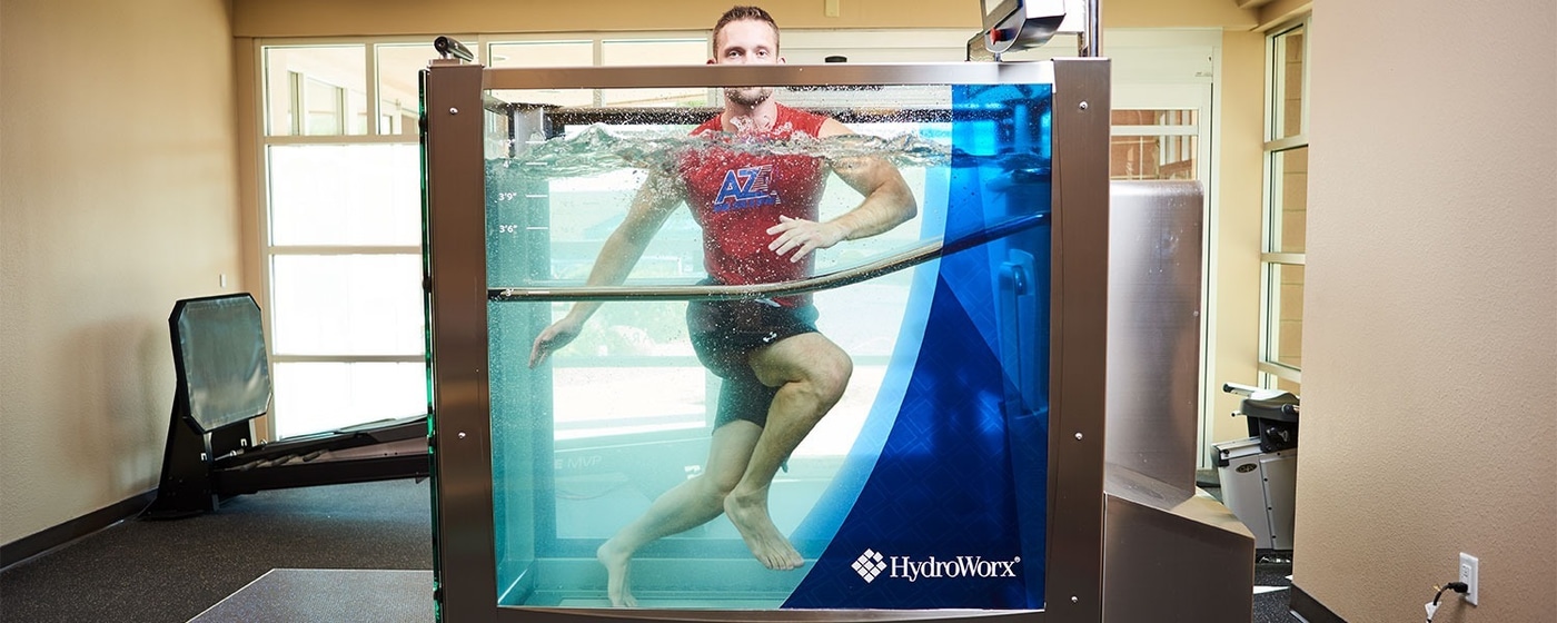 Мужчина бежит в ванне HydroWorx на фоне зала с обычной беговой дорожкой